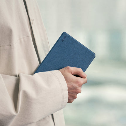 Person in a beige jacket holding an Onyx Boox Go 6 in a navy smart cover by a window