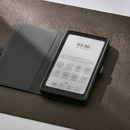 Onyx Boox Palma 2 in a dark flip cover lying open on a brown desk mat beside a cup
