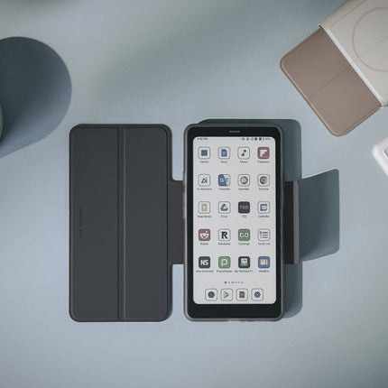 Onyx Boox Palma 2 Pro in a dark flip cover on a desk beside a cup of tea and other Palma accessories