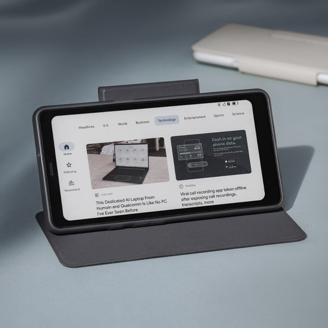 Onyx Boox Palma 2 Pro in a dark flip cover propped up like a stand on a grey surface